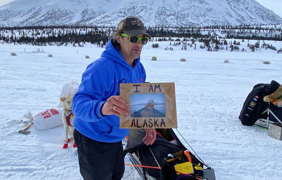 Musher Hugh Neff holds up a photo he's carrying to Nome of the late James Varsos, better know...
