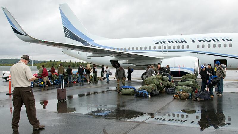 Alaska wildland firefighting crew members pull baggage off of a jet that brought them back to...